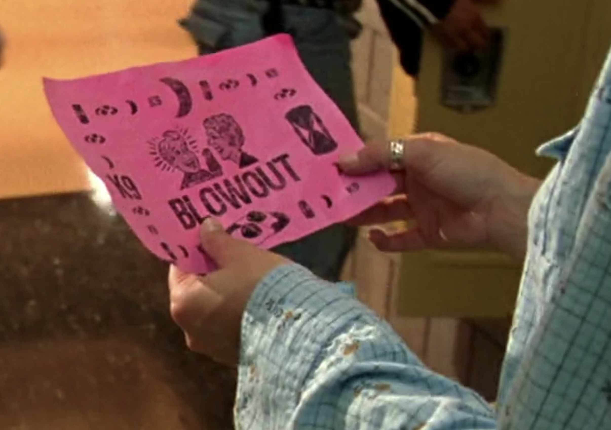 A screenshot from Veronica Mars. Veronica holds a pink piece of paper that reads BLOWOUT and is surrounded by symbols: crescent moons, eggs, "K9"
