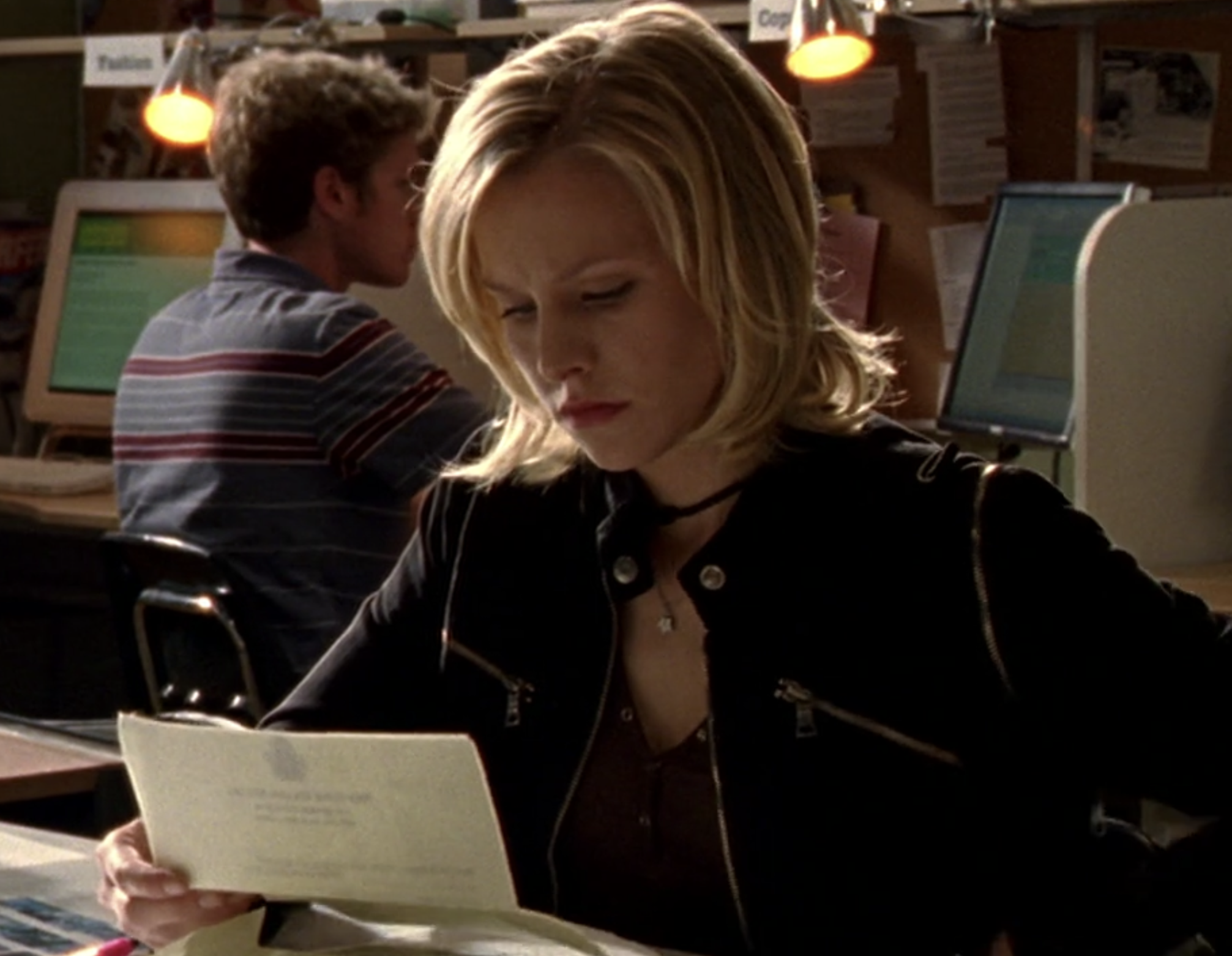 Screengrab from Veronica Mars. Veronica is in a computer lab looking at a piece of paper she is holding in her hand. She has a look of concentration on her face.