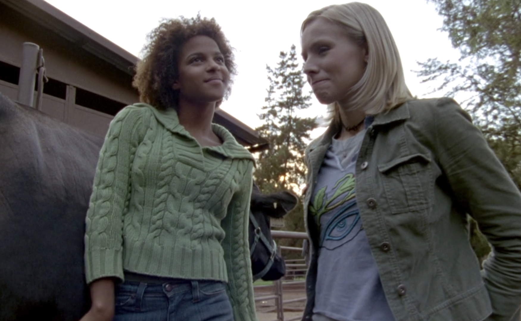 Screenshot from S1E9 of Veronica Mars. Rain and Veronica are standing at the farm next to a cow, which Rain is petting. They are talking. Rain is smiling and looking into the distance. Veronica is smiling awkwardly.