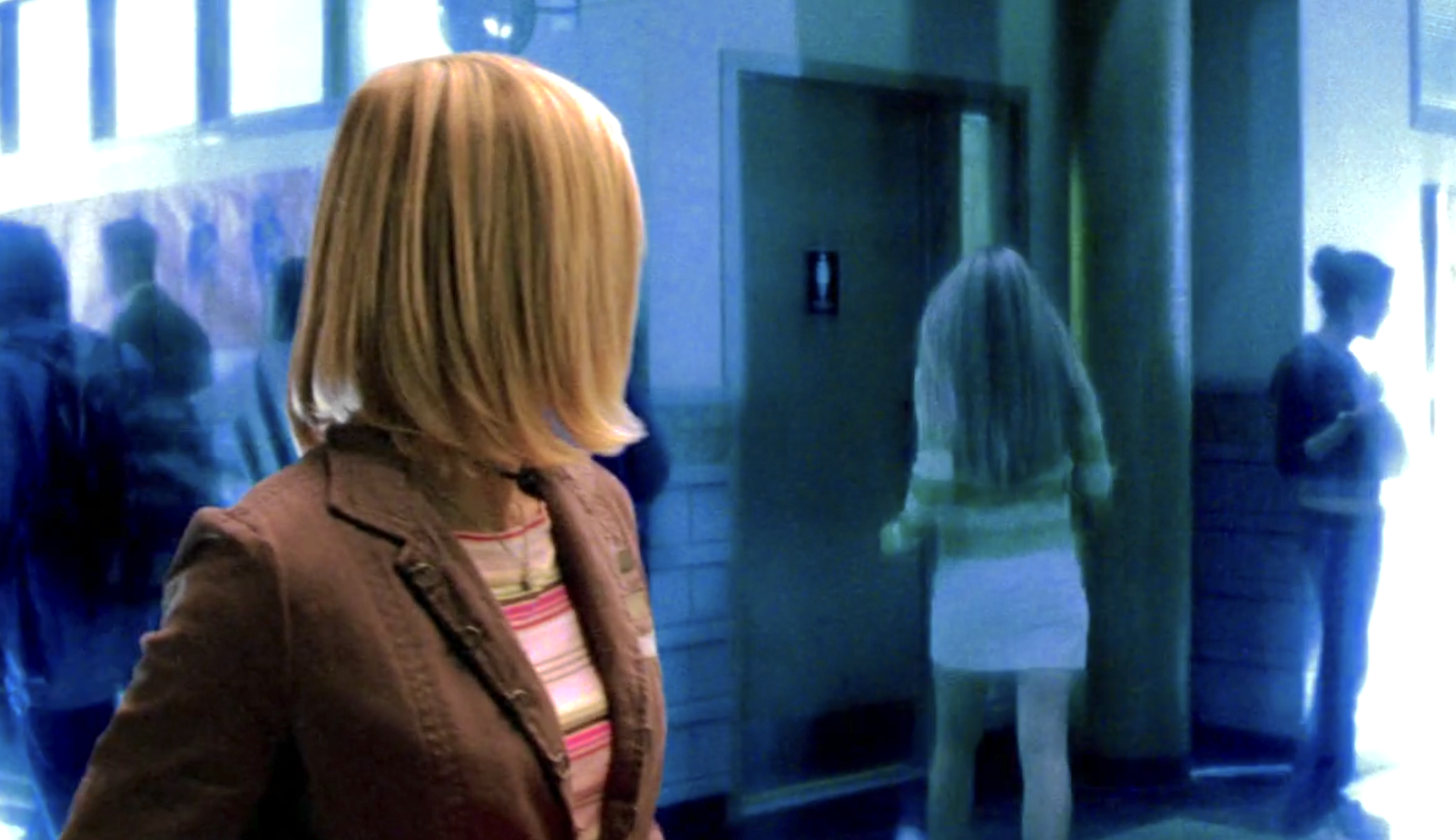Screenshot from S1E7 of Veronica Mars. It is the transition between a flashback and the present day. Present-day Veronica in sharp focus and bold color looks behind her as a flashback version of her in softer focus walks into the bathroom behind her.