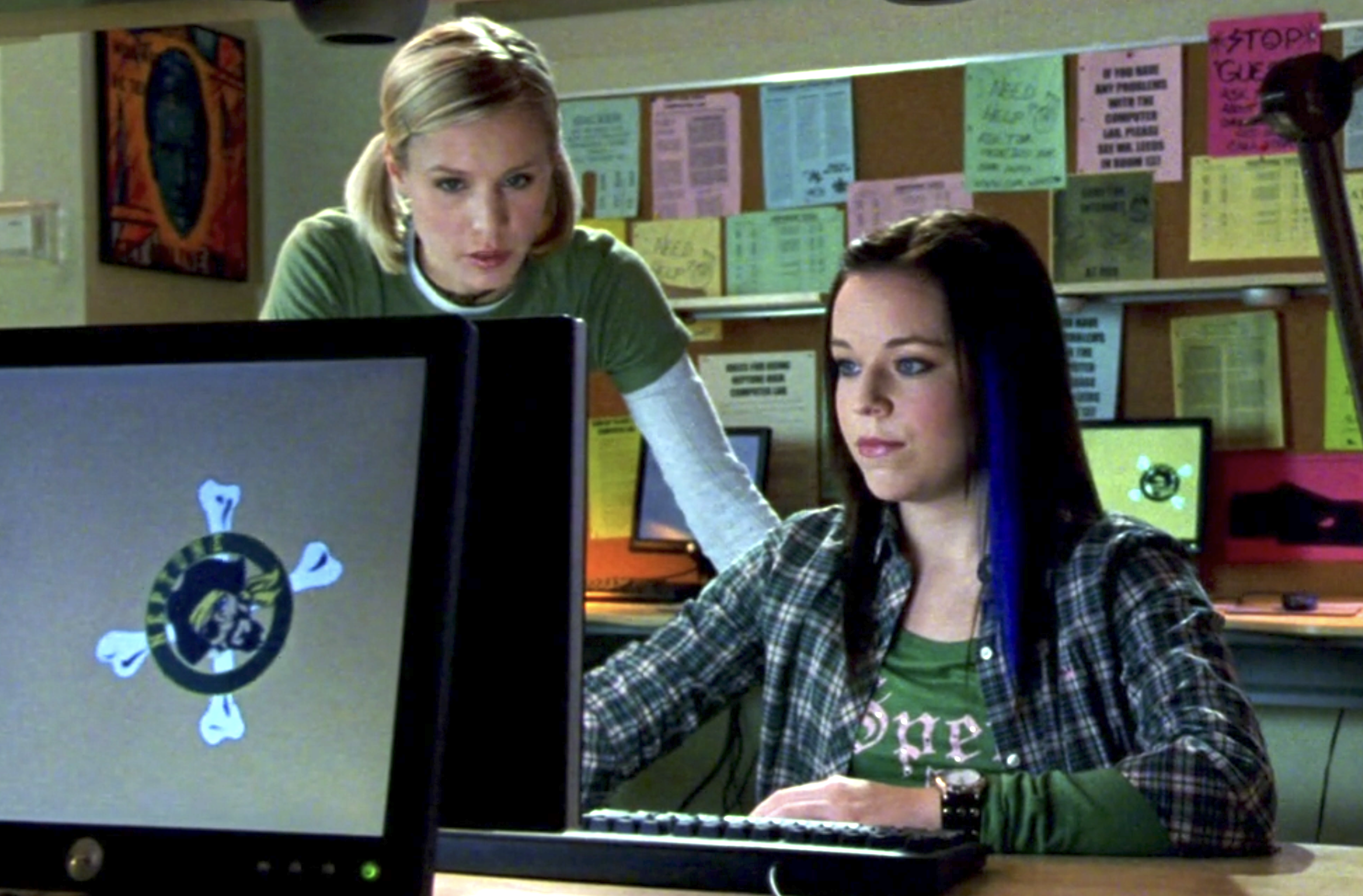 Screenshot from Veroncia Mars S1E8. Veronica stands over Mac's shoulder as Mac, seated, looks at a computer screen. They're in a classroom.