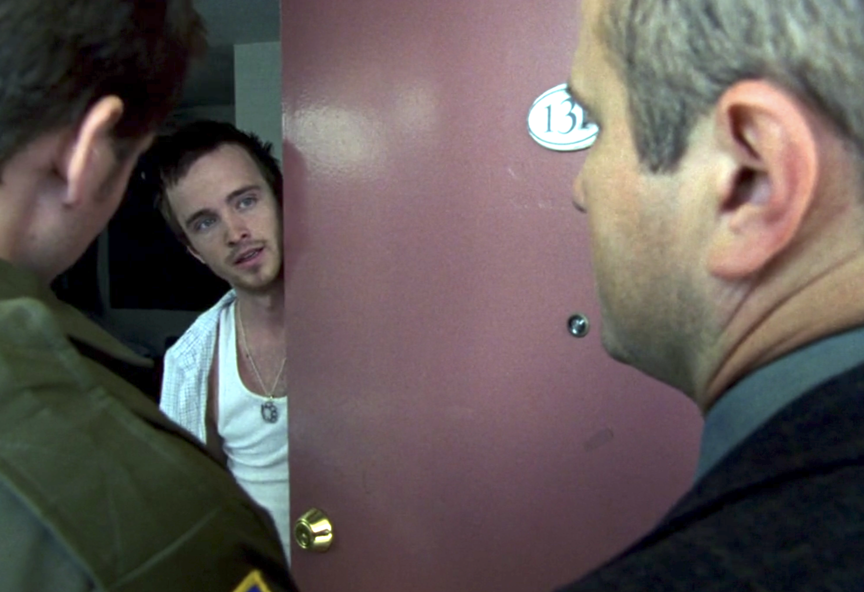 Screenshot of S1E11 of Veronica Mars. Aaron Paul in a tank top and open button down shirt has opened the door slightly and is looking out at Sheriff Lamb and Keith
