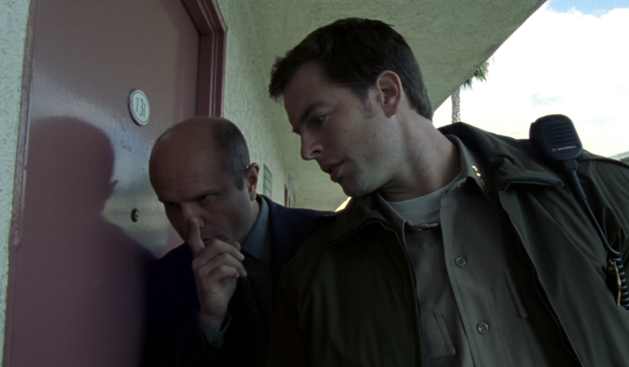 Screenshot of S1E11 of Veronica Mars. Keith and Sheriff Lamb are standing outside an apartment door listening closely at what's happening inside. Keith has his finger in front of his mouth to indicate "shh"