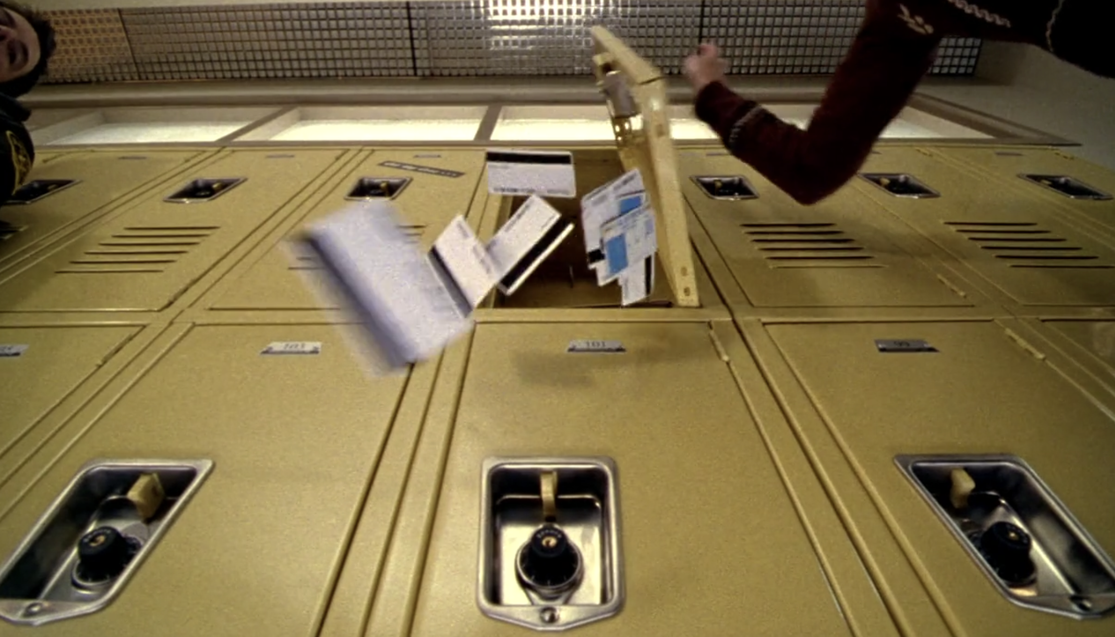 Screenshot from S1E12 of Veronica Mars. It's a shot of a bank of yellow lockers from below looking up. A bunch of fake IDs are tumbling out of an open locker on the top row.