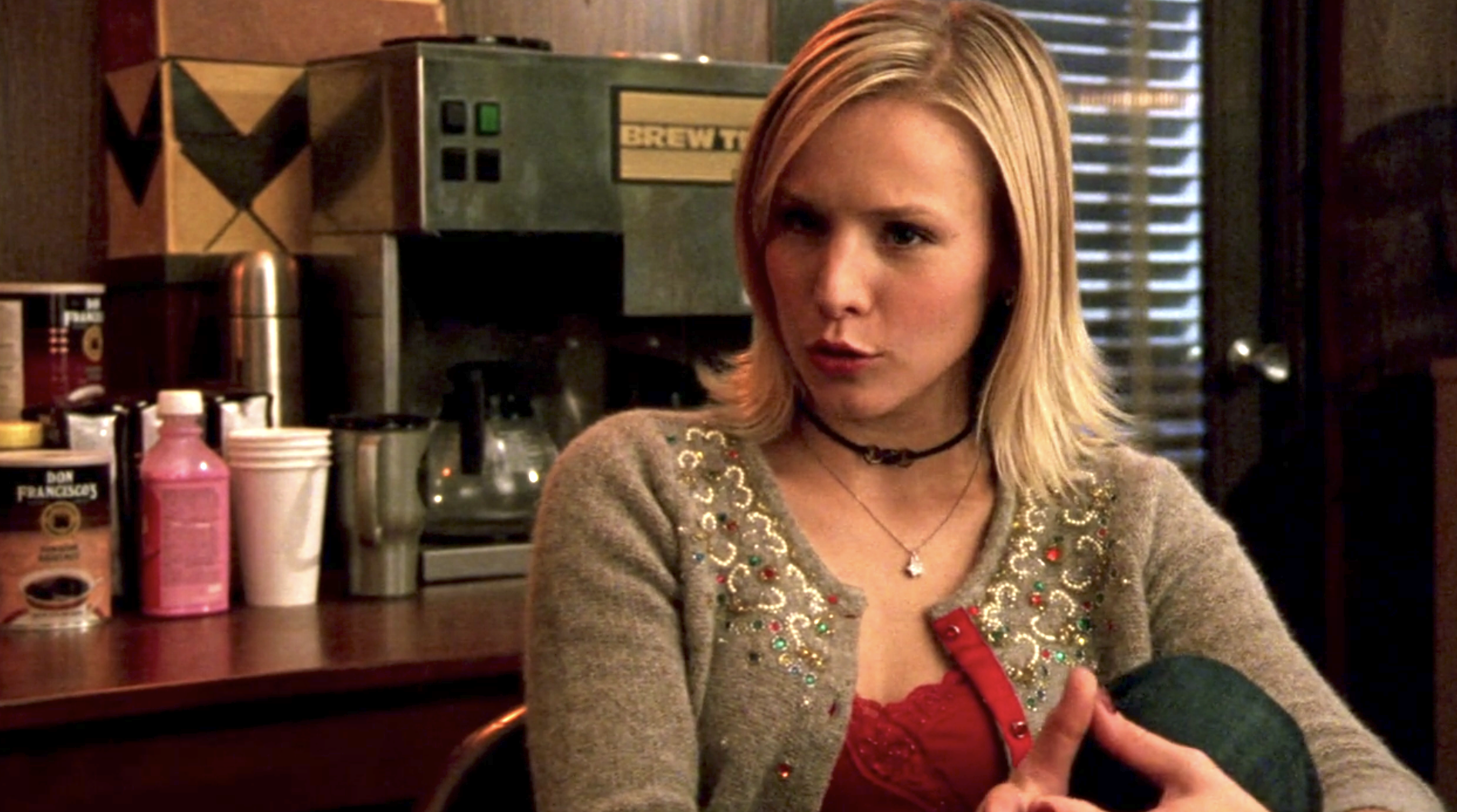 Screenshot of S1E11 of Veronica Mars. Veronica is wearing a brown sweater and red shirt and she's talking to an off-screen Leo. They're at the sheriff's department.