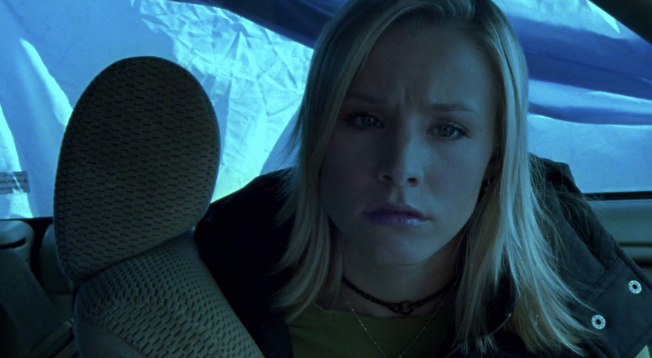 Screenshot from S1E12 of Veronica Mars. Veronica is in her car which is draped in blue cloth so everything is washed in blue light. She looks sad and concerned.