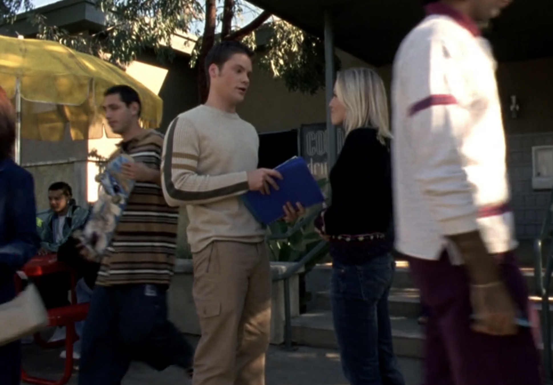 Screenshot from S1E14 of Veronica Mars. Duncan is wearing a cream-colored sweater with brown stripes and brown cargo pants. He's standing outside talking to Veronica.