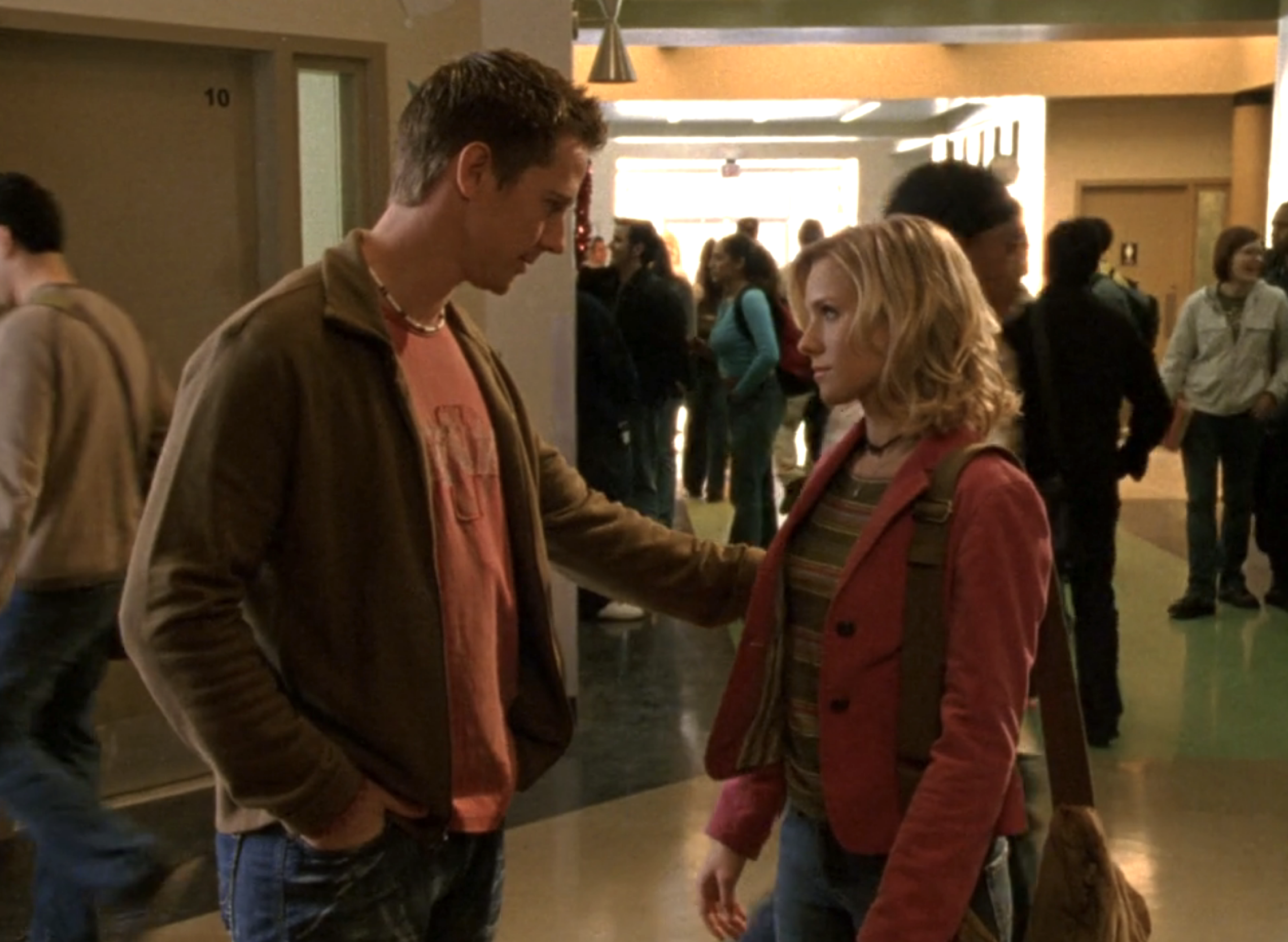 Screenshot from Veronica Mars S1E15. Logan and Veronica are standing in the hallway of Neptune High. Logan has his hand on Veronica's arm and they are making eye contact.