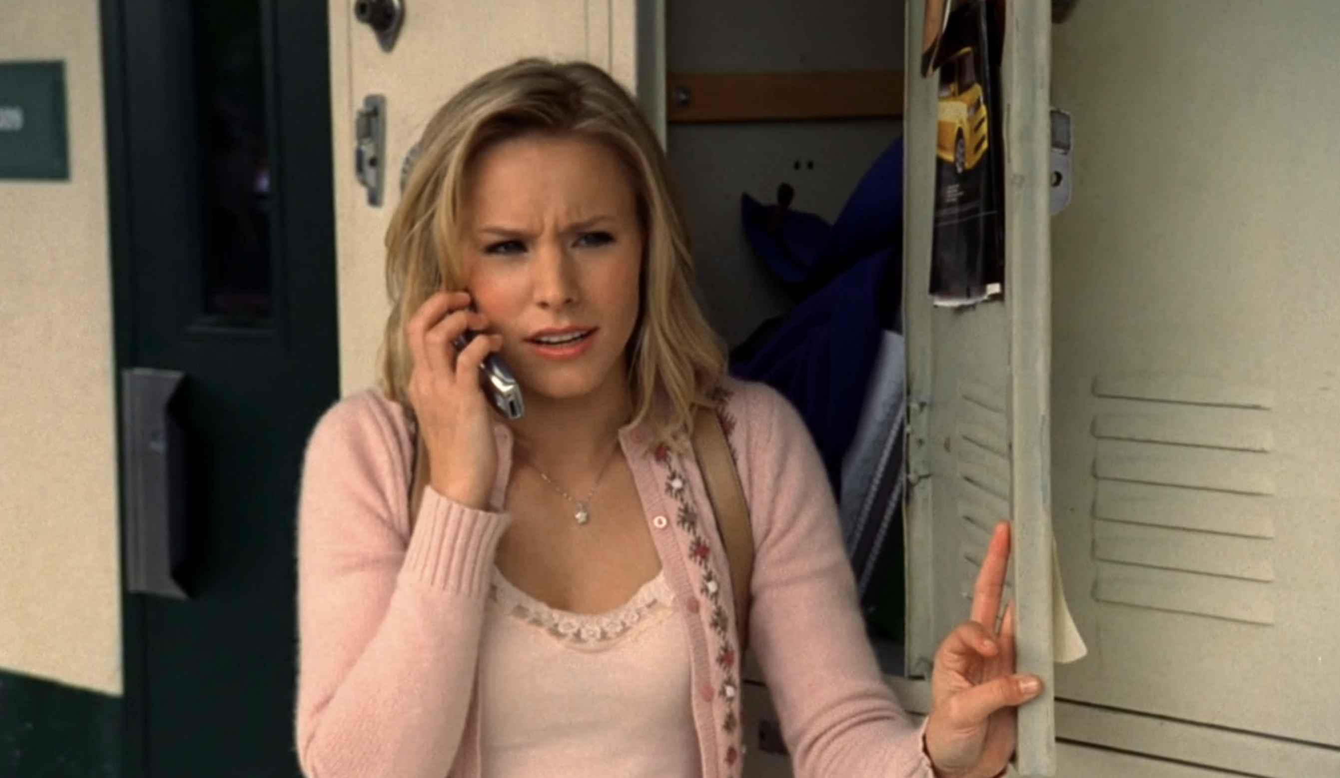 Screenshot from S1E16 of Veronica Mars. Veronica is standing by a bank of lockers with her left hand on an open locker door. She's wearing a pink cardigan and speaking into a flip phone.