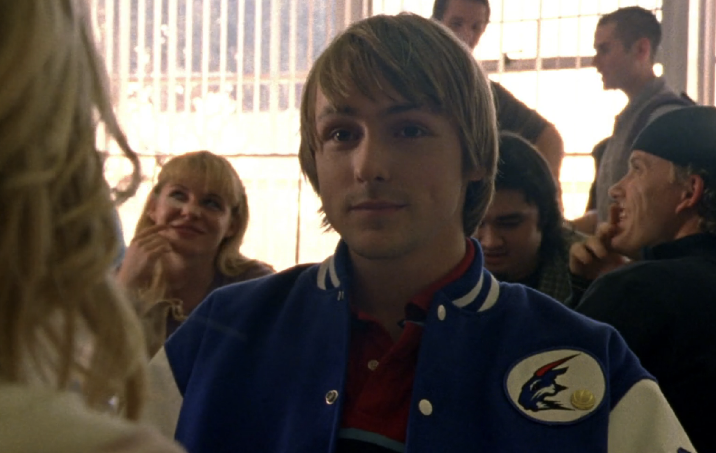 Screenshot from S1E16 of Veronica Mars. A boy with floppy hair and a Pan High varsity jacket looking sweet