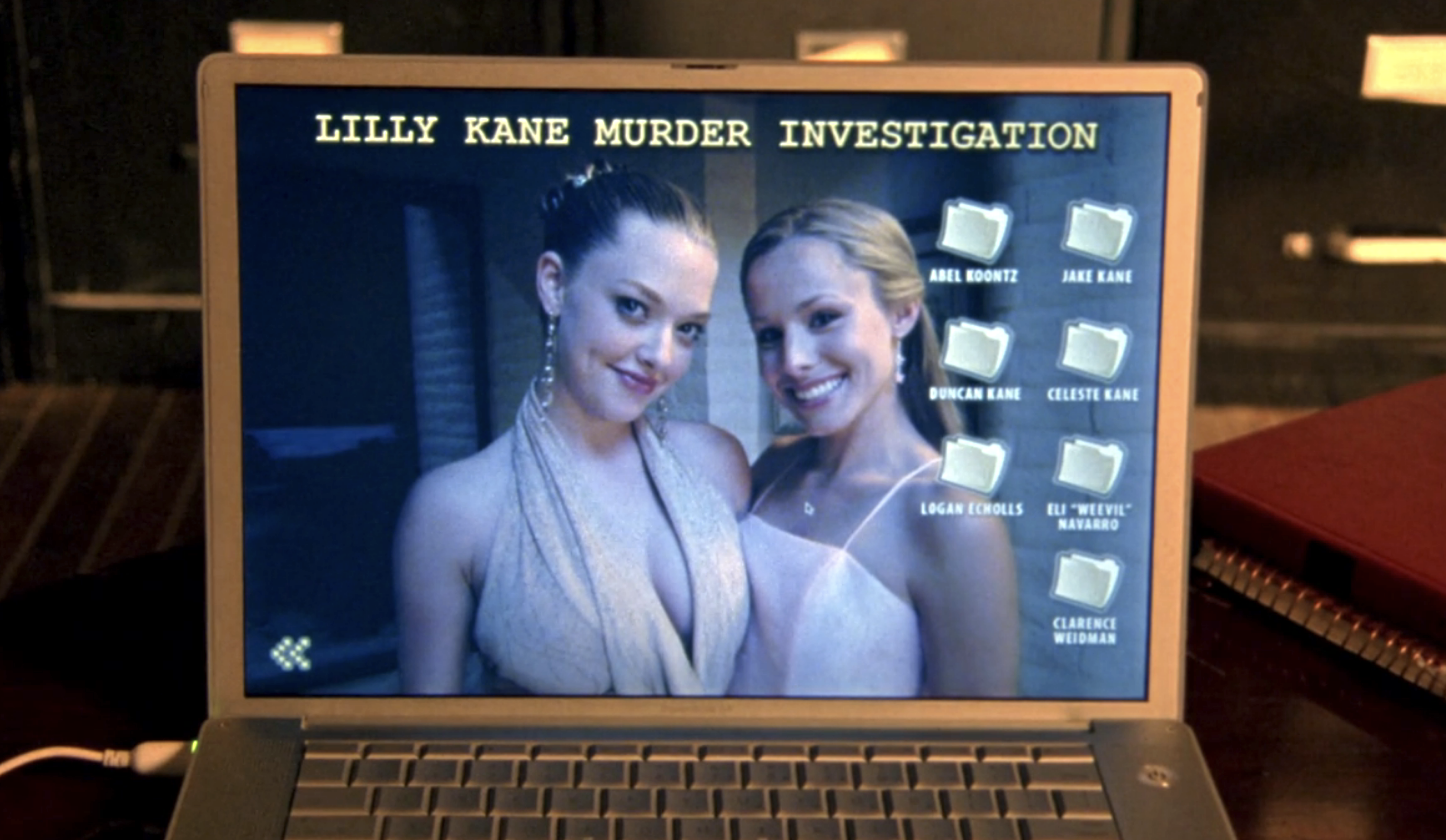 Screenshot from S1E17 of Veronica Mars. The photo is a Mac laptop whose wallpaper says "Lilly Kane Murder Investigation" with a photo of Lilly and Veronica dressed up for a dance standing and smiling together. On the desktop there are folders labeled with all Veronica's suspects in Lilly's murder.