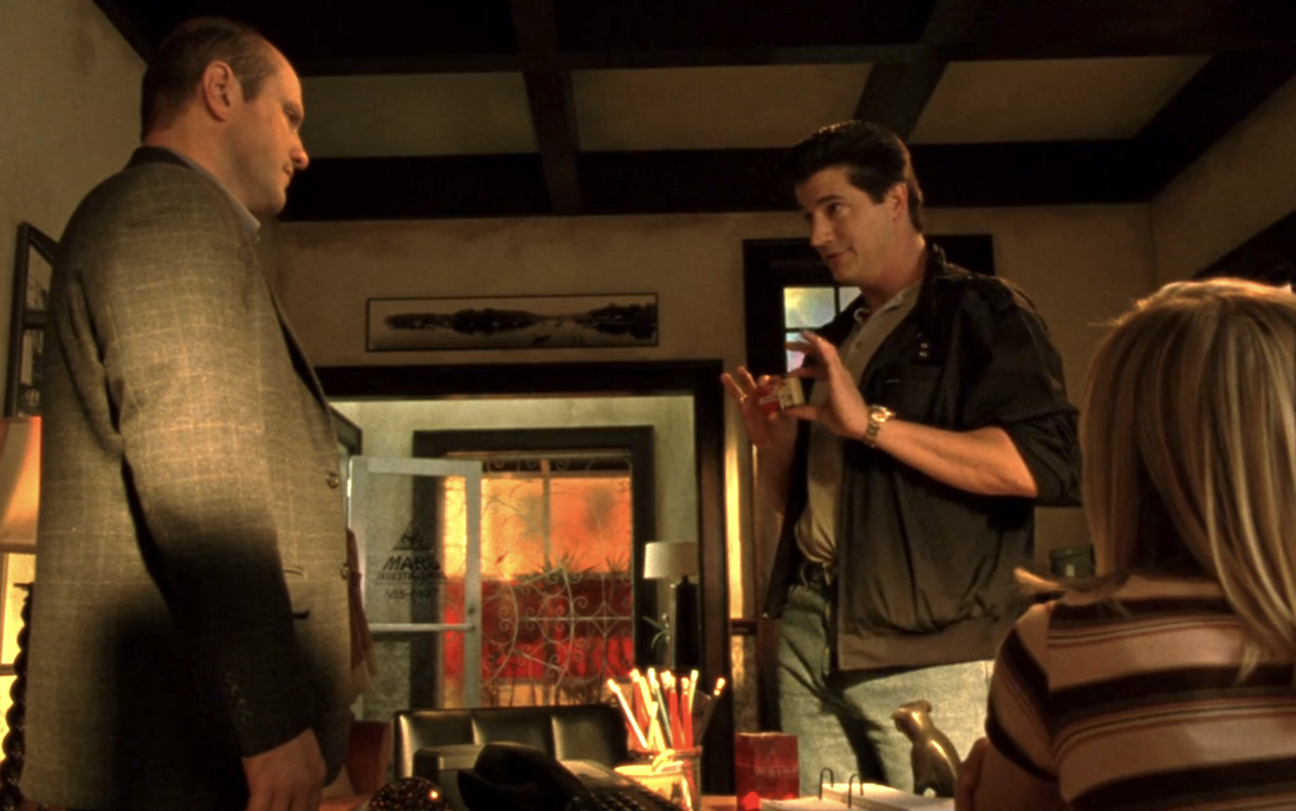 Screenshot from S1E17 of Veronica Mars. Keith and Vinny are standing in Mars Investigations. Veronica is seated, her back to the viewer. Vinny is holding his business card out to show it to Keith.