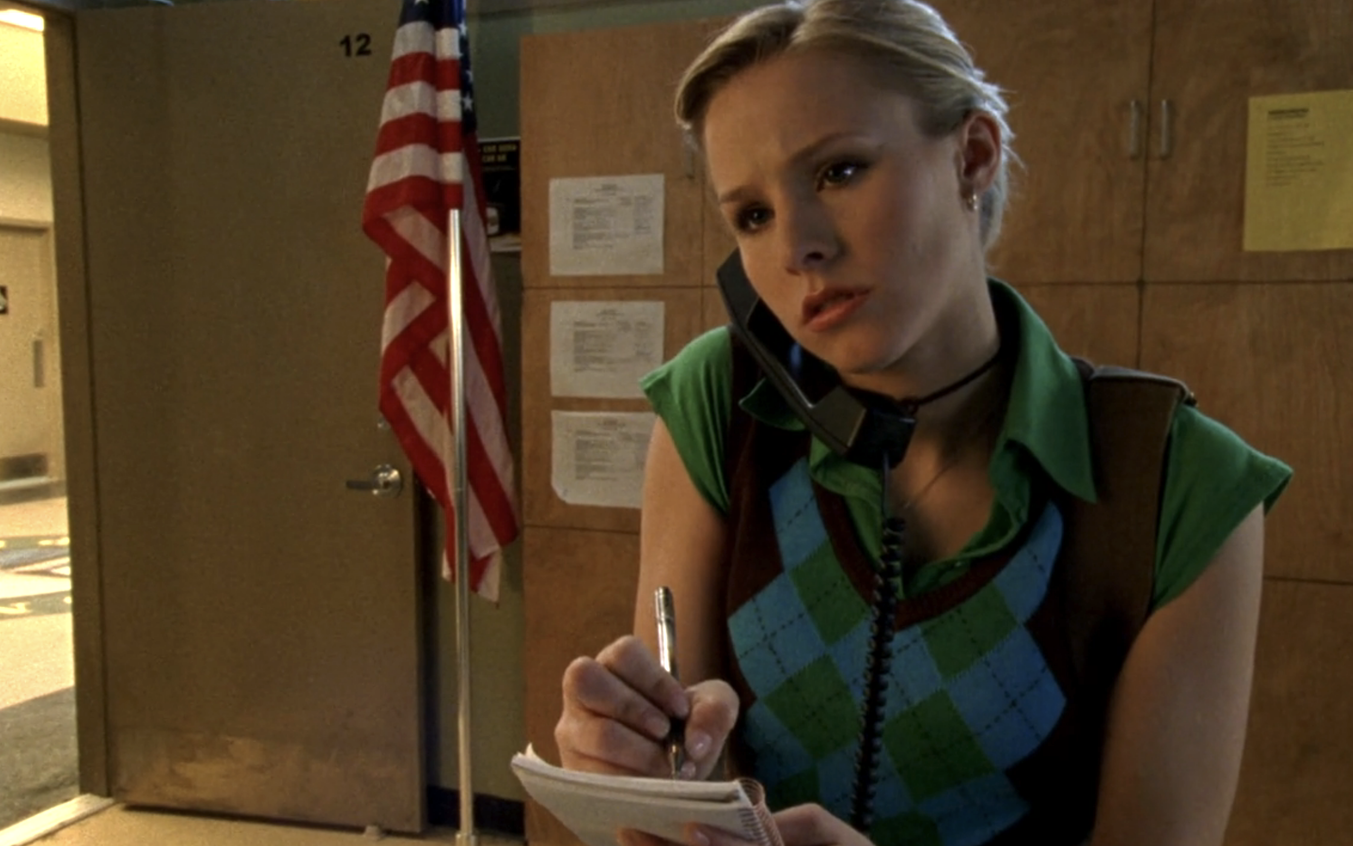 Screenshot from S1E18 of Veronica Mars. Veronica is wearing an argyle sweater vest and a green short underneath. She is taking notes in a small notebook and crading a corded telephone on her right side.