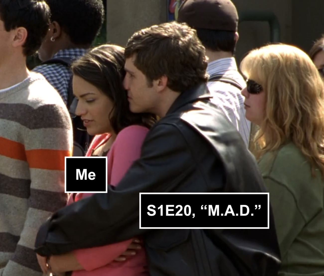 Screenshot from S1E20 of Veronica Mars. Tad, a white guy with brown hair and a leather jacket is holding Carmen, a young Latina woman in a pink swear, from behind. He's holding her snug and has his head burrowed in her hair, and she looks somehwat uncomfortable.