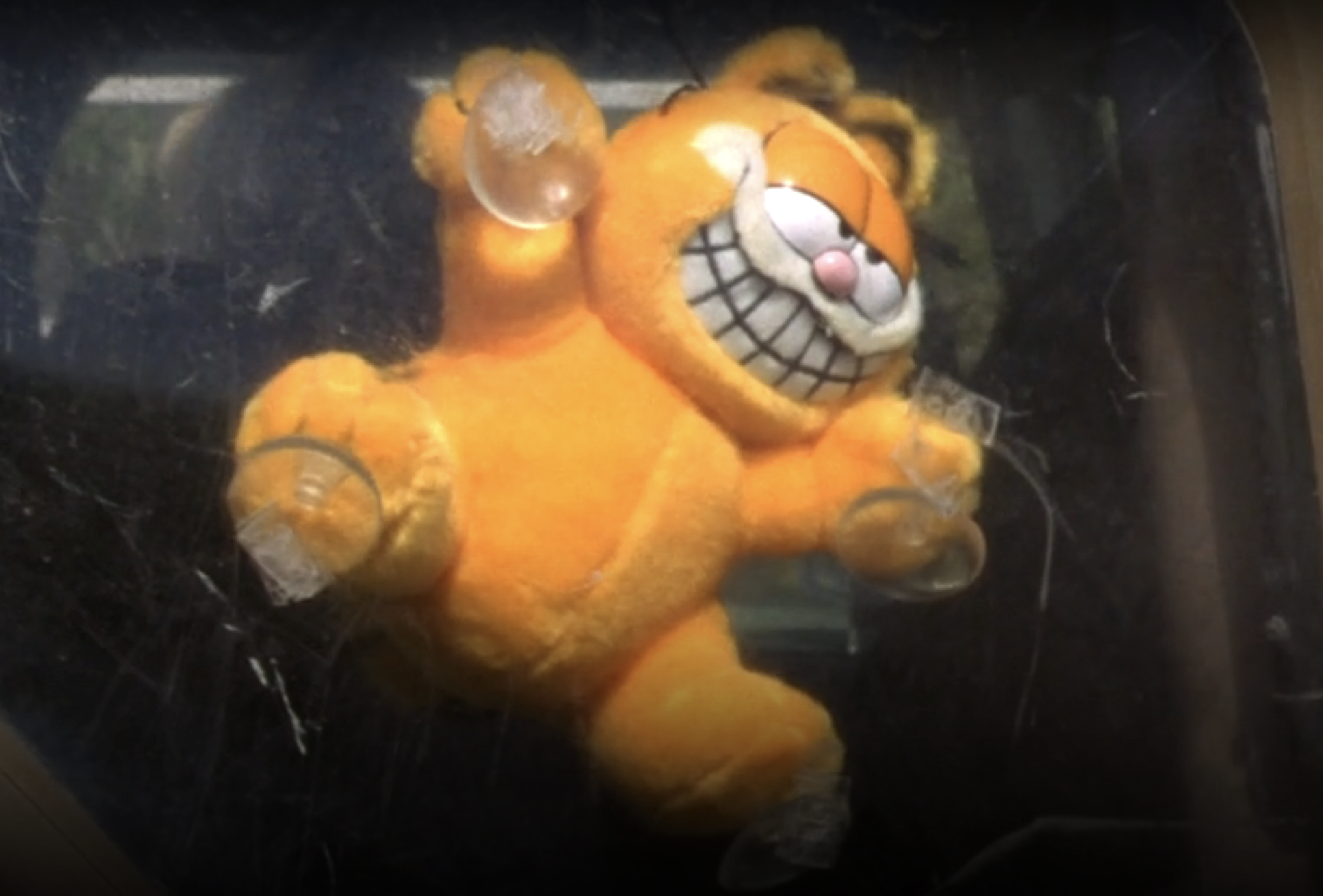 Screenshot from S1E20 of Veronica Mars. A grinning Garfield stuffed animal is stuck by suction cups to a car window.