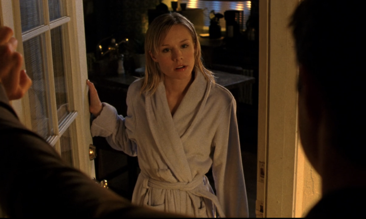 Screenshot from S1E21 of Veronica Mars. Veronica is standing in the apartment of her doorway in a gray robe looking supremely annoyed. She's looking at Logan's whose back is to us.