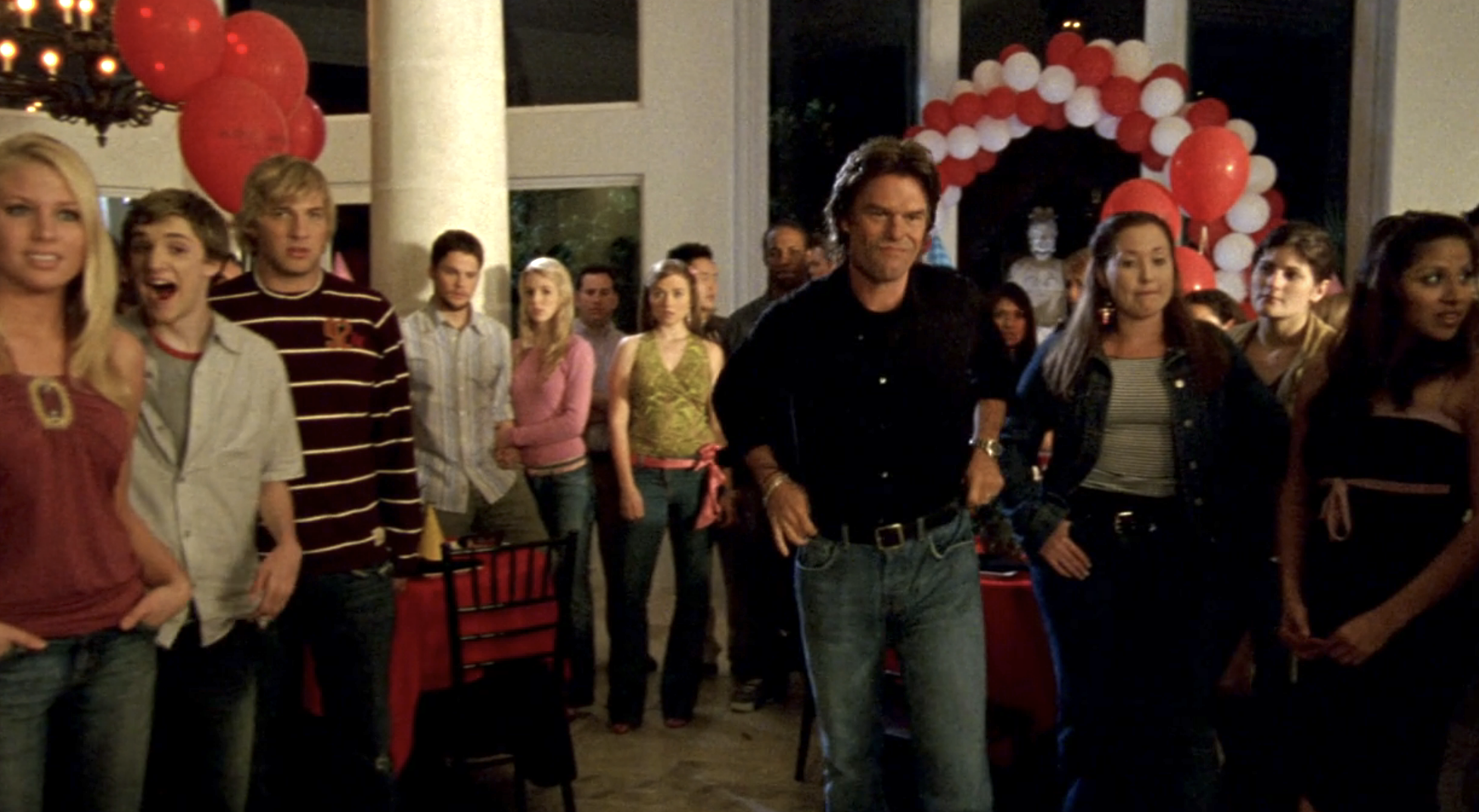 Screnshot from S1E21 of Veronica Mars. Aaron Echools is standing in his house which is crowded with Logan's friends. His hands are on his hips and he has a slight smile on his face that says "told you so."