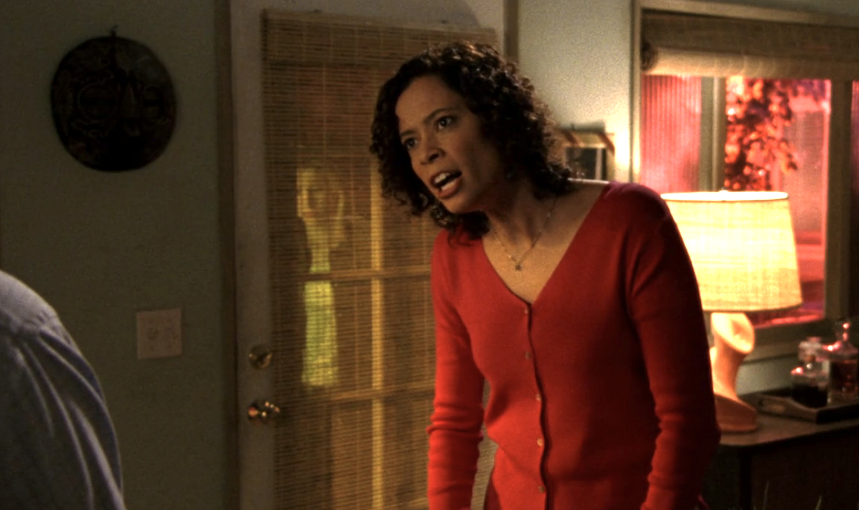 Screenshot from S1E21 of Veronica Mars. Alicia is standing in the Mars home and she is mad and seems to be speaking sharply at an off-screen Keith. She's wearing a red cardgian.