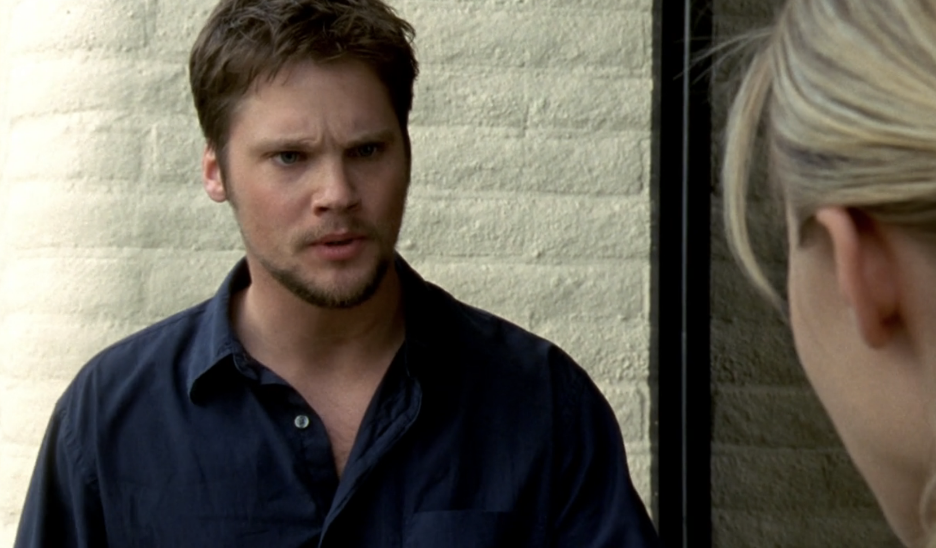 Screenshot from S1E21 of Veronica Mars. Duncan is standing outside his front door. He's wearing a dark blue shirt and has a beard and mustache. He looks upset.