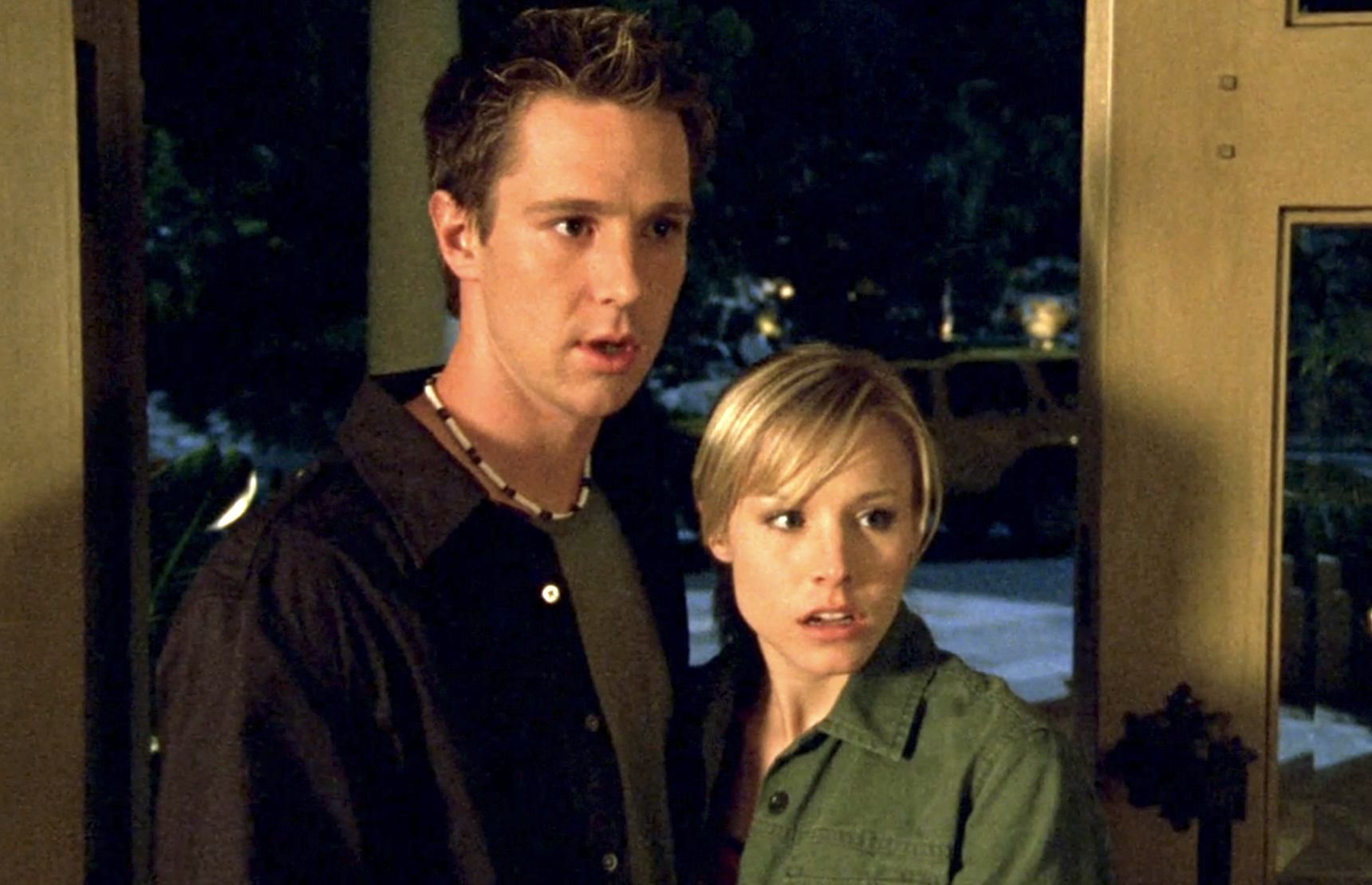 Screenshot from S1E21 of Veronica Mars. Logan in brown and Veronica in an army green. They are standing in the front door looking shocked.